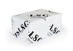 Soap bar wrapped in white paper with black text 'LSC.' and 'HANDMADE IN SMALL BATCHES' visible